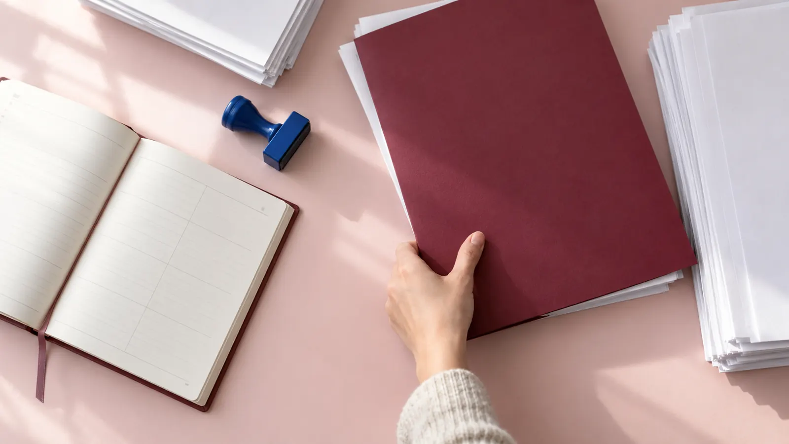 Hand verschiebt eine bordeauxrote Mappe neben einen unbeschrifteten Kalender
