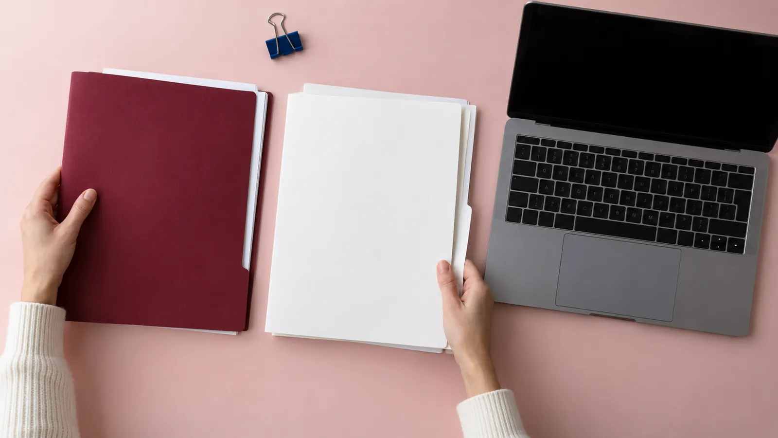 Hände ordnen Dokumentenmappen neben einem ausgeschalteten Laptop