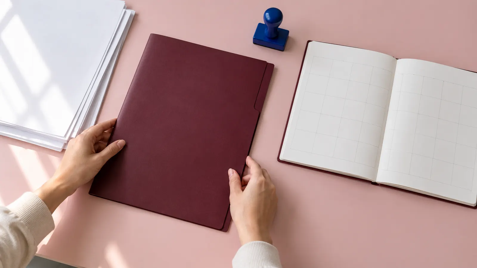 Hände legen einen bordeauxroten Ordner neben einen unbeschrifteten Papierkalender